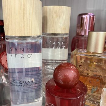 TJ Maxx - Perfume - Several Sand + Fog perfume bottles with wooden caps and decorative glass bottles are displayed on a shelf, including scents like Sol Crush and Vanilla. - Department Stores Near Me - Winchester, Kentucky