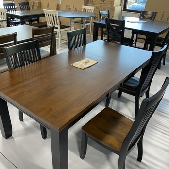 BoxDrop - A rectangular wooden dining table with black chairs is displayed in a furniture store, with additional tables and boxes visible in the background. - Mattresses Near Me - Castle Rock, Colorado