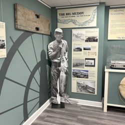Washington Historical Society - River exhibit featuring a graphic of a steamboat wheel, an image of a man with a sturgeon, life preservers, and a model of a snag boat