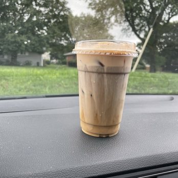 Brewpoint Craft Elmhurst - Pumpkin cold brew - A plastic cup of iced coffee with milk swirls is on a car dashboard, with a background of trees and a cloudy sky. - Coffee & Tea Near Me - Elmhurst, Illinois