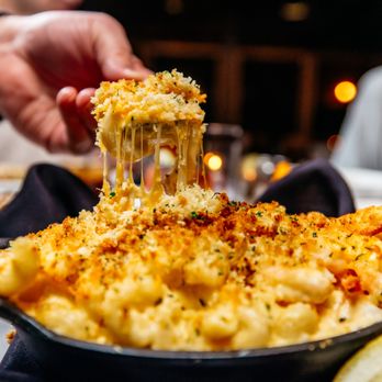 Merrill & Houston's Steak Joint - a person dipping a piece of macaroni and cheese - Steakhouses Near Me - Beloit, Wisconsin