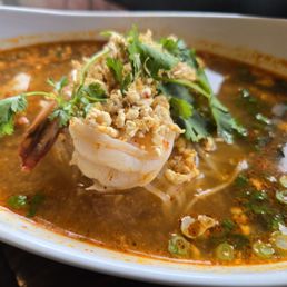 Pad Thai - A bowl of Thai soup featuring shrimp, fresh herbs, crushed peanuts, and a spicy broth, served in a white dish.