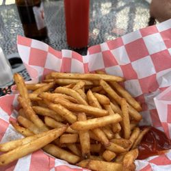 Deerfield Grille - Basket of fries sitting on red & white checkered paper & a puddle of ketchup. Bottle of ketchup & bottle of beer sitting on the table.
