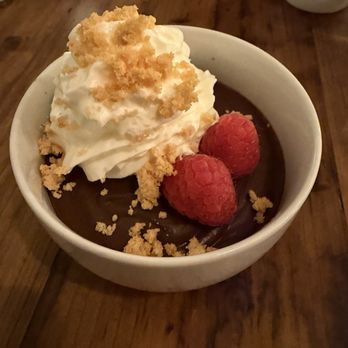 Linden + Front - Chocolate Pot de Crème (very smooth and chocolatey without being too sweet or too heavy, but too much for one person) - A bowl of chocolate pot de crème with whipped cream, two raspberries, and crumbled cookies on top, served on a wooden table. - New American Near Me - Bath, Maine