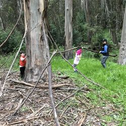 Outdoor Kids Occupational Therapy - A therapist helps 2 children build a stick fort, working on planning, coordination, and motor skills.