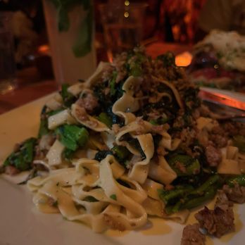 Ringolevio - Handmade Tagliatelle with Broccoli Rabe and Crumbled Sausage - A dish of handmade tagliatelle pasta topped with broccoli rabe and crumbled sausage, served on a white plate in a dimly lit restaurant. - Mediterranean Near Me - Brooklyn, New York