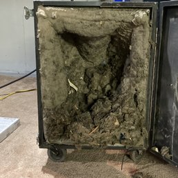 A metal cabinet on wheels with its front panel removed, exposing insulation material and debris inside, situated on a carpeted floor.