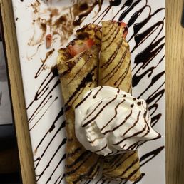Nutella Crepe - Crepes filled with strawberries, served with whipped cream and decorated with chocolate drizzle on a white plate.