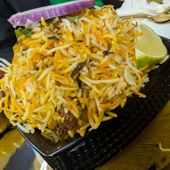 Austin Adhurs - Biryani - A plate of biryani rice with vegetables and meat, garnished with a lime wedge and onion slice, served in a black basket. - Desserts Near Me - Austin, Texas