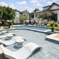 Camden Cedar Hills Apartments - Resort-style pool with in-water loungers and light blue umbrellas at Camden Cedar Hills apartments in Austin, TX