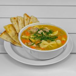 Chicken soup with mixed noodles chunks of chicken and vegetables, served with a side of Pita bread.