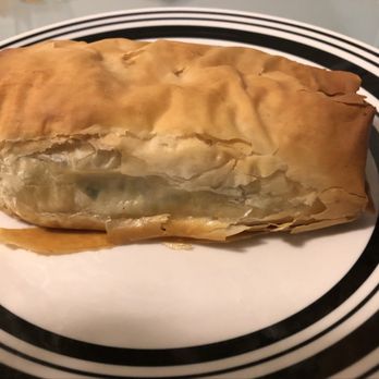 Athens Bakery - Spanakopita - A slice of spanakopita, a Greek spinach pie, is placed on a black and white plate, showing its flaky golden-brown pastry exterior. - Bakeries Near Me - Teaneck, New Jersey
