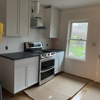 Davan Countertops - Black soapstone countertops - Kitchen featuring white cabinetry, black countertops, a stainless steel stove, and a window overlooking a backyard with outdoor furniture. - Kitchen & Bath Near Me - Franklin Park, Illinois