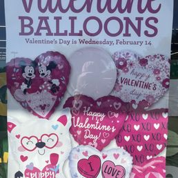 Valentine goodies inside - A collection of Valentine's Day balloons is displayed, featuring designs such as hearts, flowers, and cartoon characters like Mickey and Minnie Mouse. The balloons include messages like 'Happy Valentine's Day,' 'I Love You,' and 'Puppy Love.' The display is set up inside a Dollar Tree store, with the balloons arranged to attract customers shopping for Valentine's Day decorations and gifts.