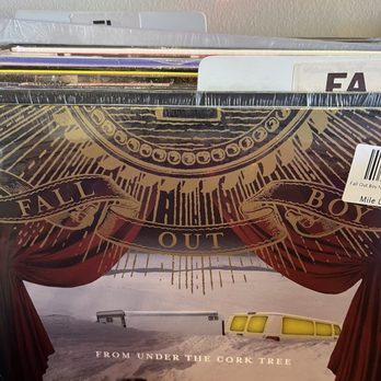Mile Long Records - From Under The Corktree by Fall Out Boy - A vinyl record album titled "From Under The Cork Tree" by Fall Out Boy is displayed among other records in a store, with a decorative cover featuring a stage curtain and a snowy landscape. - Vinyl Records Near Me - Wheaton, Illinois