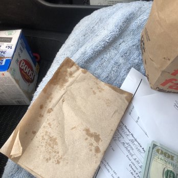 McDonald's - Just the grease and napkins they gave me.... - The image shows a car seat with a light blue towel covering part of it. On the seat, there is a stained paper bag, a box of Boost nutritional drink, some cash, and a few sheets of paper, including a receipt and a printed document. The background includes the back of a car seat with a magazine or booklet visible in the pocket. - Fast Food Near Me - Los Alamos, New Mexico