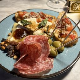 Charcuterie plate - A charcuterie plate features cured meats, cheese, green olives, and bruschetta with tomato and basil, served on a blue plate.