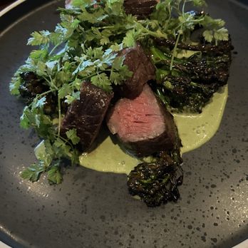 Nido - Steak - Sliced steak with a pink center, topped with cilantro, served on a black plate with green sauce and charred vegetables. - New American Near Me - Austin, Texas