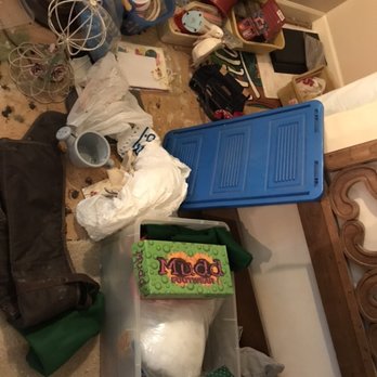 Nick Clark Auctions - taken during our NICK CLARK ESTATE SALE - The image shows a room with a variety of household items and clutter on the floor, including storage containers, decorative metal structures, a black bag, and miscellaneous objects. There are plastic bins, some with lids, and items like a mug, a small clock, and a box labeled 'Mud Footwear.' The background includes shelves with more items, such as a red container, a black box, and a decorative piece. The scene appears disorganized and contains a mix of household and decorative objects. - Auction Houses Near Me - Canton, Mississippi