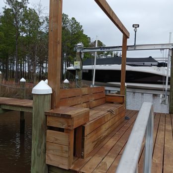 Waters Edge Construction - A wooden dock bench with sturdy posts overlooks calm water, beside a boat lift holding a covered speedboat... - General Contractors Near Me - Chesapeake, Virginia