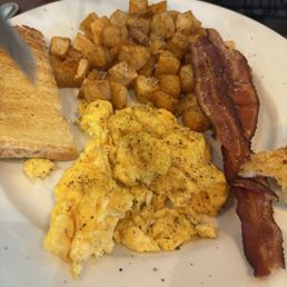 Egg breakfast - A breakfast plate featuring scrambled eggs, crispy bacon, roasted diced potatoes, and a slice of toasted bread.