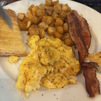 Mimosas - Egg breakfast - A breakfast plate featuring scrambled eggs, crispy bacon, roasted diced potatoes, and a slice of toasted bread. - American Near Me - Denver, Colorado