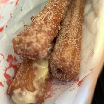 Xurro - Churros - Two churros coated with cinnamon sugar, one filled with cream, placed in a paper wrapper at a churro stand or shop. - Desserts Near Me - Burbank, Illinois