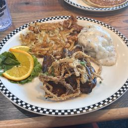 Meatloaf with onion straws, mashed potatoes, hash browns, and orange slice