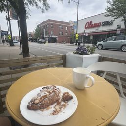 A table on the sidewalk outside of Lost Larson in Andersonville. On the table is a "large" London Fog (tea latte) and an almond croissant.