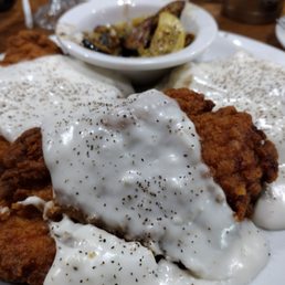 Chicken fried steak - A plate of chicken fried steak with white gravy and black pepper, accompanied by roasted potatoes in a small bowl.