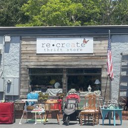 Various furniture and household items are arranged outside the Re·Create thrift store, including chairs, a stroller, and decorative objects.