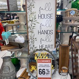A vertical decorative sign with the quote 'full house, full hands, full heart' is displayed among various home decor items at a store, with a clearance sign indicating 66% off.