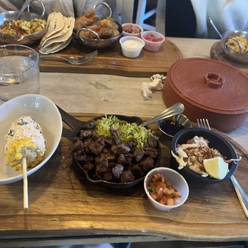 Centro Mexican Kitchen - Steak tacos- but more like "fajita" style. The corn was amazing. - The image shows a Mexican meal served on a wooden tray, including grilled steak pieces with rice, a small bowl of salsa, and a side of guacamole with lemon. Additional dishes and condiments are visible on the table, along with a glass of water and other plates of food in the background. - Mexican Near Me - Boulder, Colorado