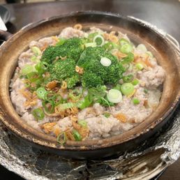Hot Pot Rice - A clay pot filled with rice, topped with salted fish, pork, broccoli, and chopped green onions, served in a restaurant with a dark wooden table.