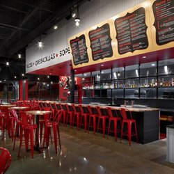 Taco Bamba Herndon - Interior of restaurant facing the kitchen. Large menu boards over the counter which has over a dozen bar seats also visible a...