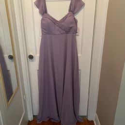 Original dress - A lavender-colored formal dress with cap sleeves and pleated bodice details hangs on a wooden hanger in front of a white door.