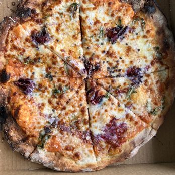 Tocoi Feed Mill - Amazing fresh pizza made at the Feed Mill - A cheese pizza with a slightly charred crust, topped with melted cheese, basil leaves, and slices of prosciutto, served in a cardboard pizza box. The pizza appears freshly baked with a golden-brown crust and bubbling cheese. - Livestock Feed & Supply Near Me - Saint Augustine, Florida