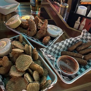 Northside Tap - Chicken Tenders, Mozz Sticks and fried pickles - Three baskets of fried appetizers—potato chips, fried pickles, and mozzarella sticks—are on a bar counter, accompanied by dipping sauces and a glass of beer. - Bars Near Me - Valparaiso, Indiana