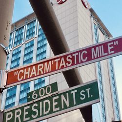 Domino Sugar Baltimore - The Charm'tastic Mile famed street sign in front of downtown skyline of buildings and hotels.