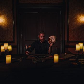 The Dark Seance - a man sitting at a table with a skull - Dinner Theater Near Me