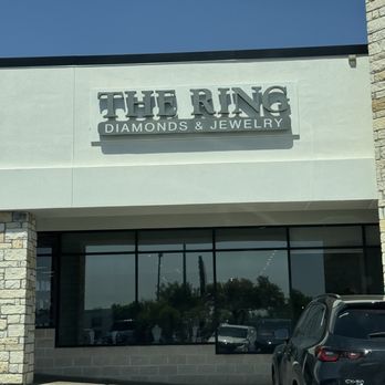 The Ring Austin - The image shows the exterior of The Ring Diamonds & Jewelry store with a prominent sign on the building facade and a parking lot in front. - Jewelry Near Me - Austin, Texas