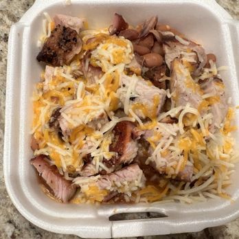 Duke City BBQ - BBQ Bowl - A foam takeout container contains pieces of barbecue meat topped with shredded cheese and beans. The container is placed on a speckled granite countertop, and the food appears to be a barbecue dish with cheese and beans as toppings. - Barbeque Near Me - Albuquerque, New Mexico