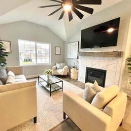 A spacious living room features a large window, a fireplace with a marble surround, and contemporary furniture including sofas and an armchair.