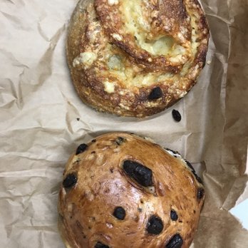 The Cheeseboard Collective - What we ordered: Sourdough Cheese Roll and Chocolate Thing - A cheese roll and a chocolate chip bun are placed on crumpled brown paper, showcasing their baked textures and toppings. - Bakeries Near Me - Berkeley, California