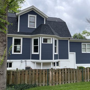 Pacer Decorating - Side - A two-story house with blue exterior siding, white window frames, and a dark shingled roof, enclosed by a wooden fence. - Painters Near Me - Wheaton, Illinois