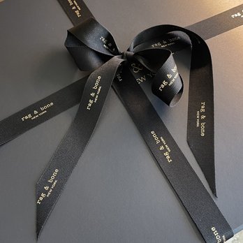 rag & bone - Beautifully wrapped package - A black rectangular gift box is wrapped with a black ribbon that has 'rag & bone' printed on it, placed on a marble surface. - Men's Clothing Near Me - Chicago, Illinois