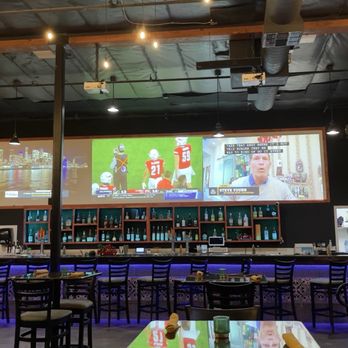 Mango Haus Lounge  - The bar - A bar with a long counter illuminated by blue lighting, multiple chairs, and large screens showing sports and news, with artwork on the walls. - New American Near Me - Tehachapi, California