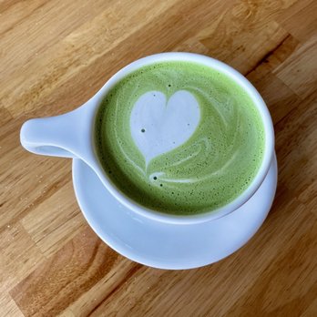 Doughfee - Matcha Latte - A green matcha latte with foam art in the shape of a heart in a white ceramic cup on a wooden surface. - Coffee & Tea Near Me - Jacksonville, Florida