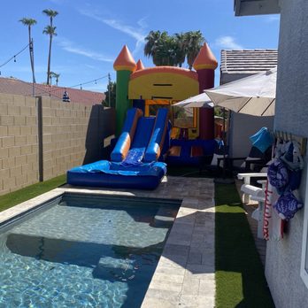 Get Bouncey - A backyard scene featuring a small rectangular pool, an inflatable castle with slides, and outdoor seating with umbrellas, enclosed by a brick wall. - Bounce House Rentals Near Me