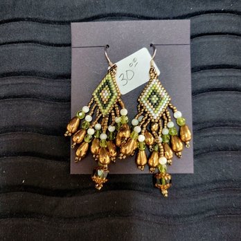Beaded Iris - Pair of beaded earrings featuring diamond-shaped beadwork with dangling gold, white, and green beads, displayed on a dark background. - Arts & Crafts Near Me - Albuquerque, New Mexico